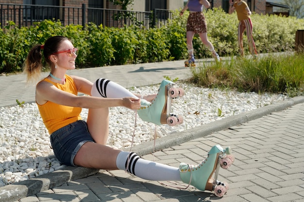 Smiling teenage girl tying shoelace of roller skate while sitting on the ground