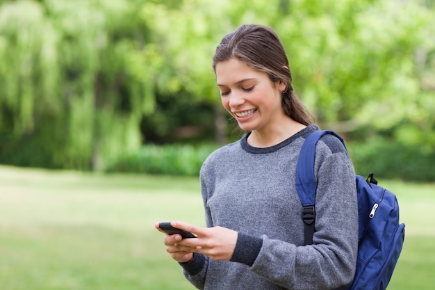 Adolescente sorridente che utilizza il suo cellulare mentre ricevendo un testo