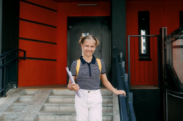 Photo a smiling teenage girl with a backpack and a folder in her hands goes down the stairs