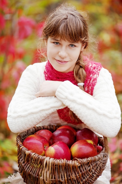 가 정원에서 사과 바구니를 들고 웃는 십 대 소녀. 가을 수확기에 과일을 먹는 유아. 아이들을 위한 야외 활동. 건강한 영양