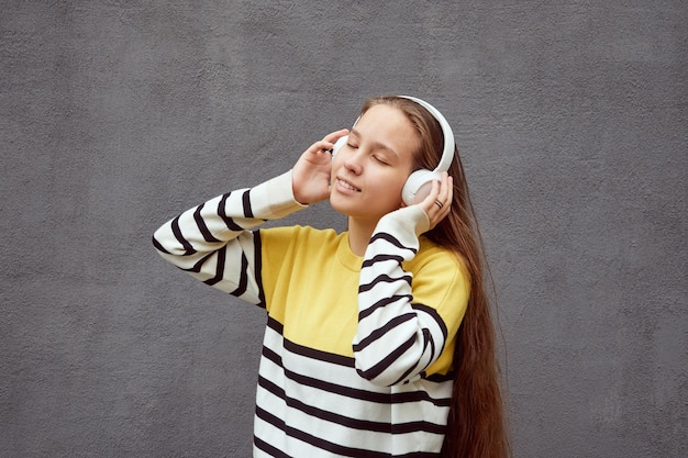 Photo smiling teenager girl listening to music in wireless headphones on gray background