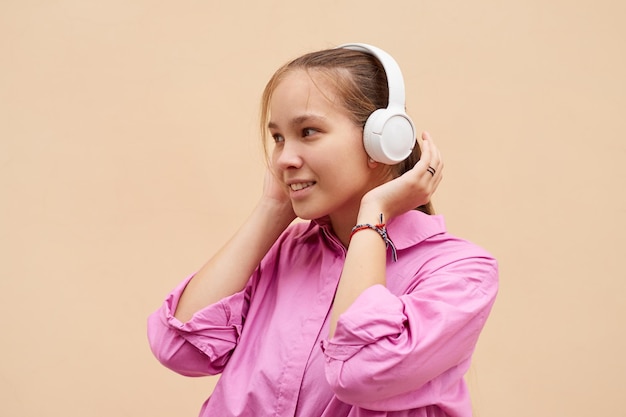 Photo smiling teenager girl in a pink shirt listens to music in headphones