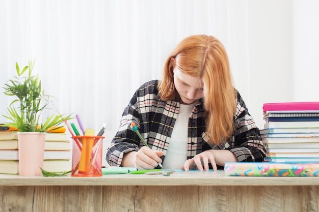 Smiling teenager student girl doing homework at home, education and school concept