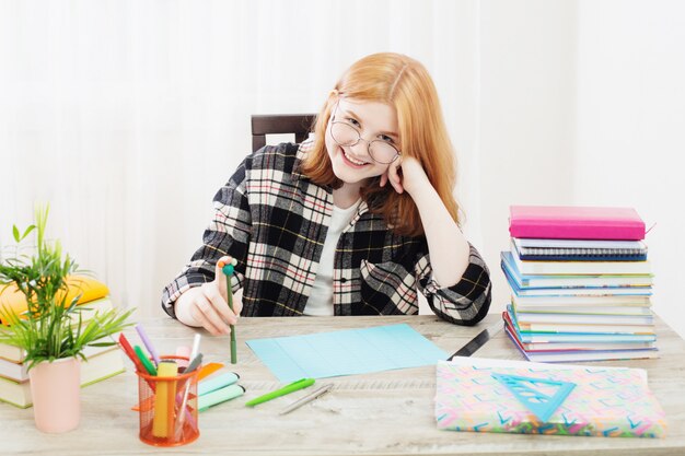 Smiling teenager student girl in glasses doing homework at home, education and school concept