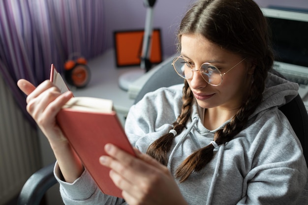 A smiling teenager with glasses reads a school reading at home