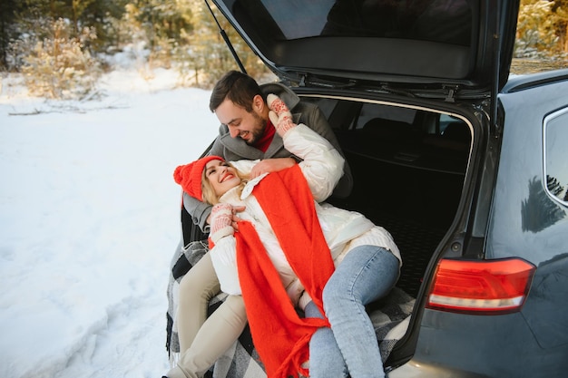 Sorridere insieme. la bella coppia trascorre il fine settimana in campagna durante l'inverno. seduto sulla parte posteriore dell'auto moderna.