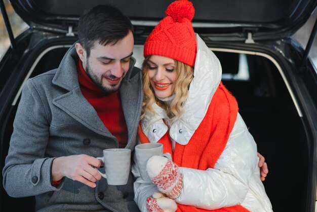 smiling together nice couple have weekend at countryside at winter time sitting on the rear part of modern car