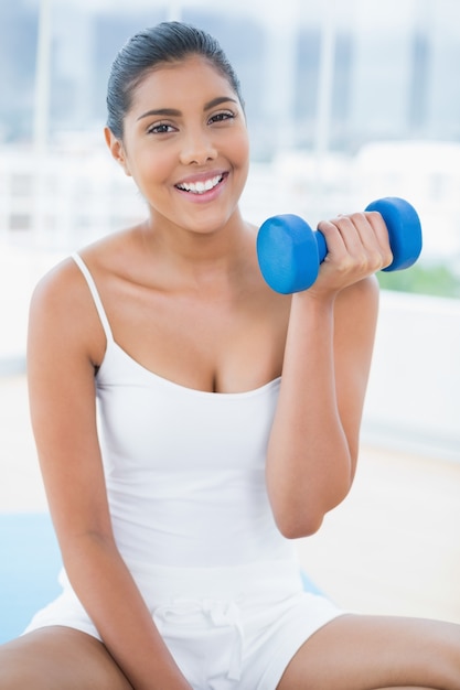 Sorridere castana tonificato che si siede sul pavimento con i dumbbells