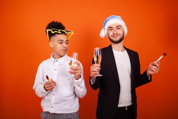 Smiling two international friends in formal wear with a Santa hat and star glasses with party horns