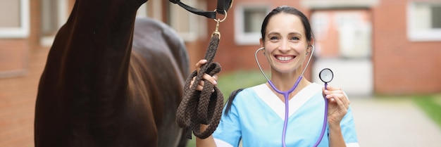 Il veterinario sorridente con il cavallo sta tenendo il concetto di servizi veterinari dello stetoscopio