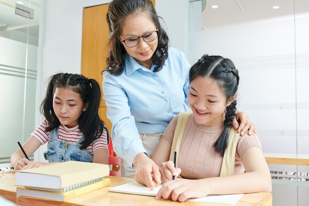 Smiling Vietnamese school teacher telling student to correct mistake in copybook