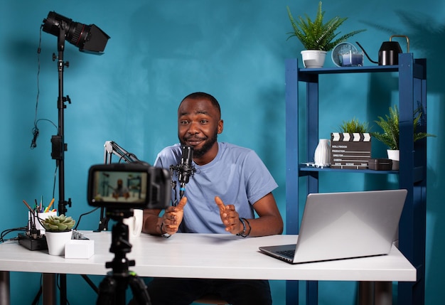 Smiling vlogger talking with audience in front of recording\
digital video camera during online live show. content creator\
interacting with fanbase in studio looking at dslr live video\
podcast setup.