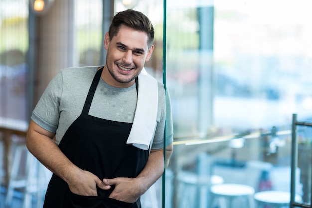 Foto cameriere sorridente che si appoggia porta di vetro in caffetteria