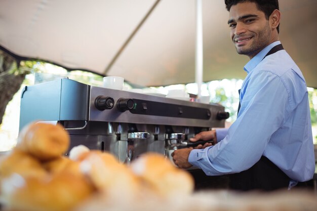 Smiling waiter making cup of coffee from espresso machine