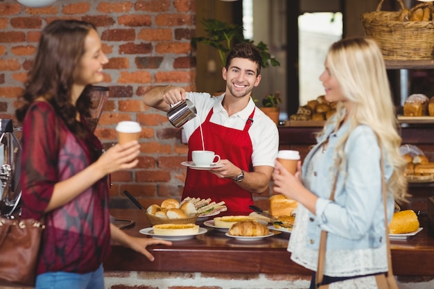 Cameriere sorridente che versa latte in una tazza di caffè