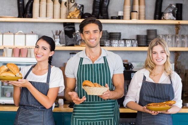 Smiling waiter and two waitresses holding plate of bread rolls