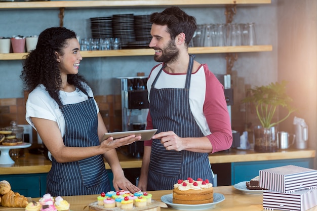 Smiling waiter and waitress using digital tablet at counter