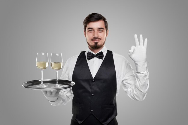 Smiling waiter with glasses of wine showing ok gesture