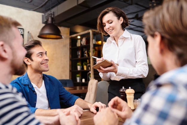 Cameriera di bar sorridente che prende le note mentre prendendo ordine