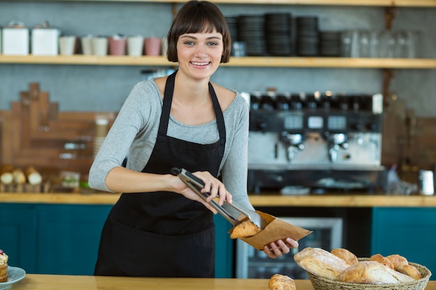 Smiling waitress packing croissants in paper bag at cafe