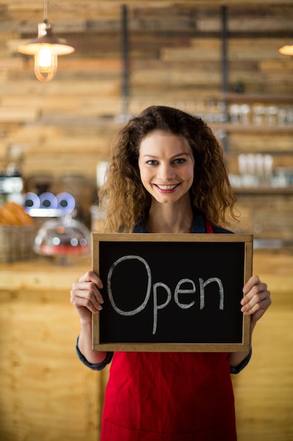 Smiling waitress showing slate with open sign in coffee