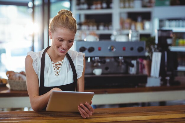 Smiling waitress standing at counter using digital tablet