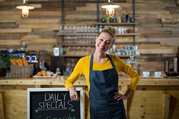 Foto cameriera di bar sorridente che sta con il bordo del menu in caffè