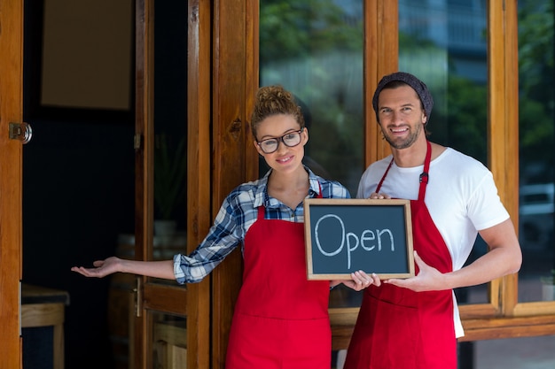 Smiling waitress and waiter standing with open sign board outside coffee