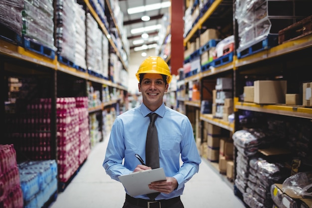 Smiling warehouse manager writing on clipboard in warehouse