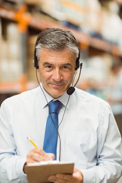 Smiling warehouse manager writing on clipboard