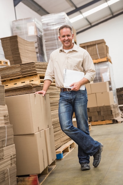 Smiling warehouse worker leaning against boxes