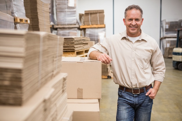 Smiling warehouse worker leaning against boxes