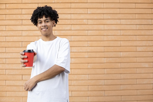Smiling wavy haired guy holding a red coffee cup wearing a white Tshirt