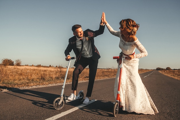 写真 日没時に街の外の道路に沿ってスクーターに乗って笑顔の結婚式のカップル。