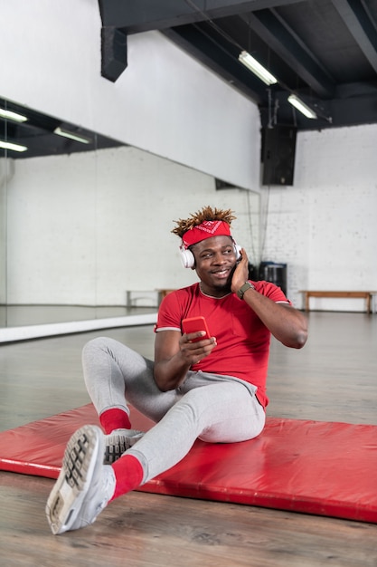 Smiling well shaped young man resting on sportive mat while wearing red t shirt