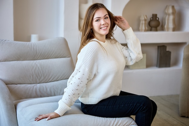 Smiling white woman sits on sofa indoors