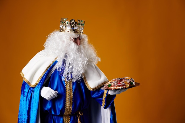 smiling wise man holding a roscon de reyes in his hand on an orange background