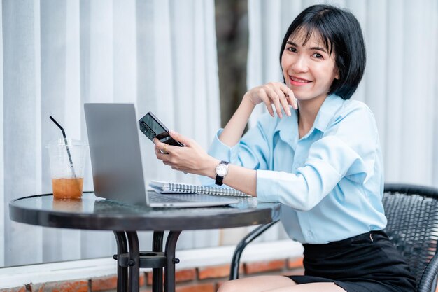 Smiling with dental braces asian freelance people Businesswoman writing message on smartphone casual working with laptop computer with a coffee cup mug at the cafeBusiness Lifestyle