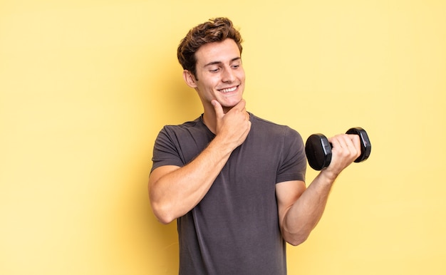 Smiling with a happy, confident expression with hand on chin, wondering and looking to the side. dumbbell concept