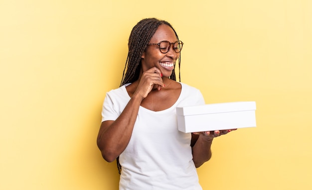 Smiling with a happy, confident expression with hand on chin, wondering and looking to the side and holding an empty box