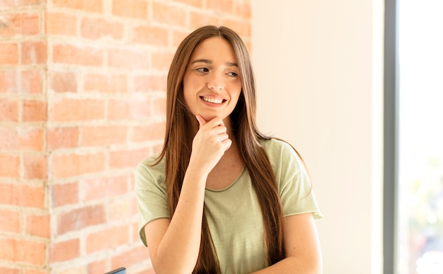 smiling with a happy, confident expression with hand on chin, wondering and looking to the side