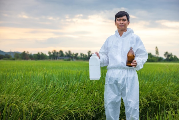 Фото Радостно улыбаясь в сельской местности таиланда фермер держит рисовые поля и бутылку с пестицидом или химическим удобрением в руке, глядя в камеру.