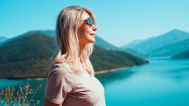 Smiling woman against mountain landscape and lake. Zhinvali reservoir lake landscape with mountains . The main Caucasus ridge.