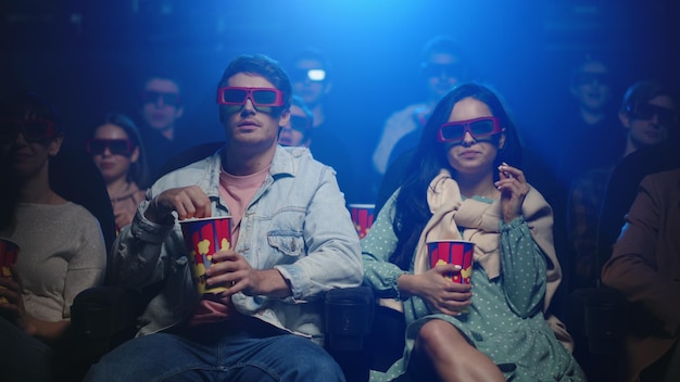 Фото Улыбающаяся женщина и веселый мужчина смотрят комедийный фильм в кинотеатре радостные друзья смеются в кинотеатре молодая пара ест попкорн в темном зале люди смотрят на экран в 3d-очках