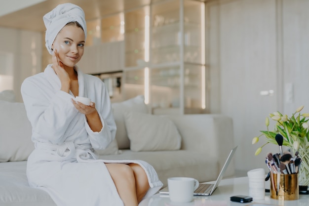 smiling woman applies nourishing cream on face