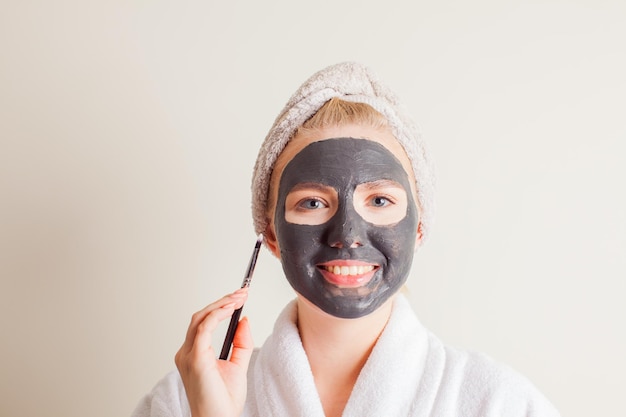 Smiling woman applying black charcoal mask on face at home