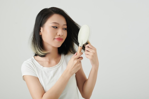 Улыбающаяся женщина расчесывает волосы пластиковой щеткой
