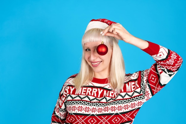 Smiling woman in christmas sweater holding ornament eye