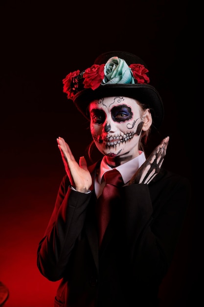 Smiling woman in costume with skull make up celebrating traditional mexican holiday with goddess of death costume. La cavalera catrina culture celebration with skull body art over black background.