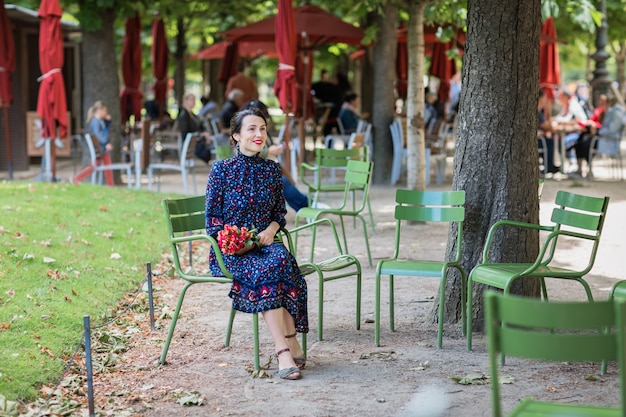 公園の椅子に座っている紺色のドレスを着た笑顔の女性